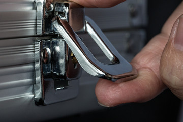 Extreme close-up of human hand opening or closing metal briefcase