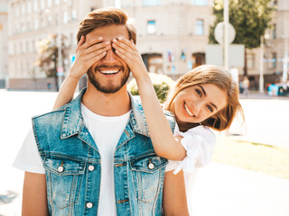 Smiling beautiful girl and her handsome hipster boyfriend. Woman covering her man eyes with hands. Happy cheerful family. Hugging loving couple standing outdoors.Guess who concept