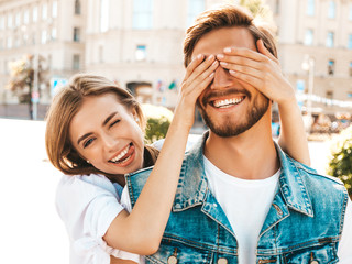 Smiling beautiful girl and her handsome hipster boyfriend. Woman covering her man eyes with hands. Happy cheerful family. Hugging loving couple standing outdoors.Guess who concept
