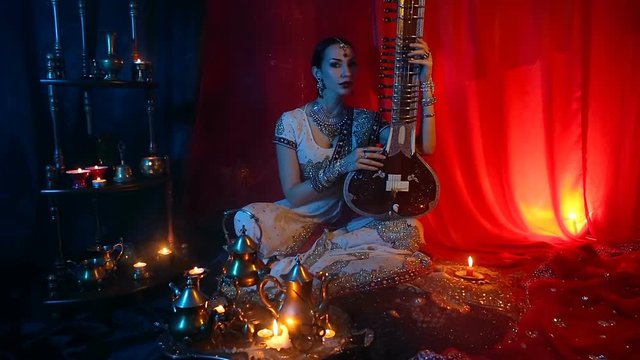 Beautiful young indian woman in traditional Sari clothing with Oriental Jewelry Playing the Sitar.
