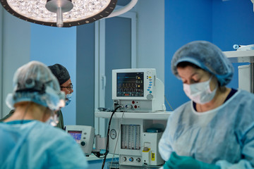 Surgeon performing cosmetic surgery in hospital operating room. Surgeon in mask wearing loupes...