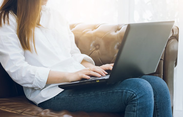 Naklejka premium Young asian woman sitting on sofa and using laptop working in cafe