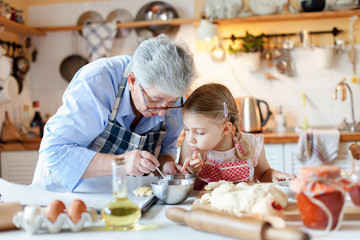 Family is cooking in cozy kitchen at home. Grandmother and child are making italian food and meal. Senior woman and little girl are baking. Cute kid is helping to prepare dinner. Children chef concept