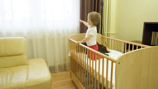 Lovely child stay in bed, toddler point with finger to lighted window, kid show the light, release