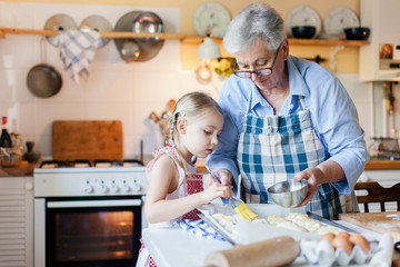 Family is cooking in cozy home kitchen. Grandmother and child are using oven. Retired woman and little girl are baking french pastries. Cute kid is helping to prepare dinner. Children chef concept.