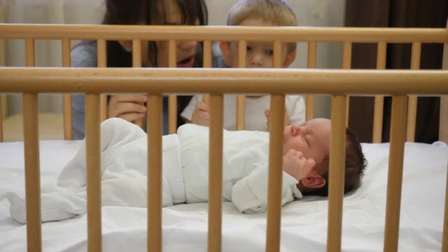 Mother and baby brother looking at newborn sleeping in a child crib