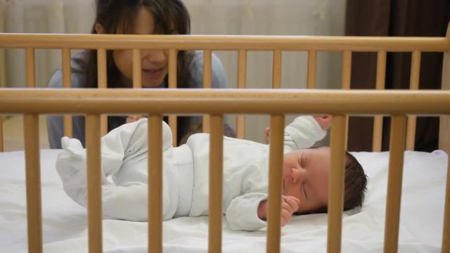 Young mother with toddler brother looking at newborn baby sleeping in a wooden child crib