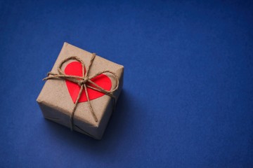 Single gift box. Wrapped in brown craft paper and tie by hemp cord. Heart carton decorative cards. Blue paper background. Text space. 