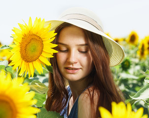 A beautiful teenage girl in a hat with a wide brim stands in a field with sunflowers