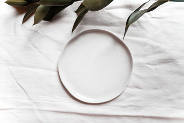 Authentic ceramic table setting mock up with linen napkin top view. Wedding holiday table setting mockup background for wallpaper, design, lettering, cards, blogs. Tableware with green branch.