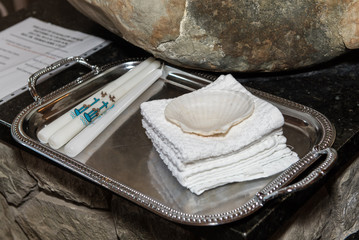 Tray containing Paschal Candles, towels, and shell are arranged neatly and ready for the Baptism ceremony at the altar.