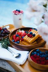breakfast by the pool with fruits and berries in wooden bowls: waffles, milkshake, strawberries, raspberries, blueberries, cherries, orange slices, lemon, lime, watermelon and pineapple