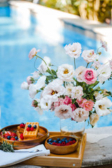 breakfast by the pool with fruits and berries in wooden bowls: waffles, milkshake, strawberries, raspberries, blueberries, cherries, orange slices, lemon, lime, watermelon and pineapple