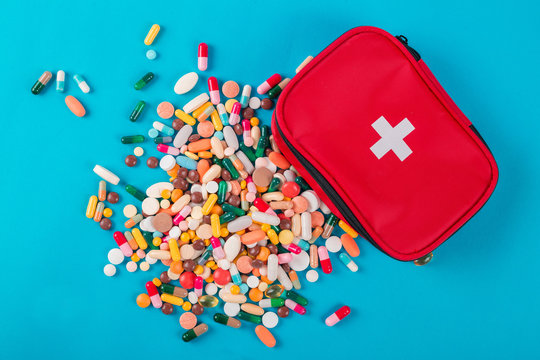 Assorted pharmaceutical medicine pills, tablets and capsules and first aid kit on blue background - Powered by Adobe