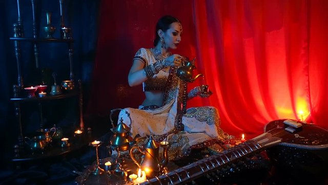 Beautiful young indian woman in traditional Sari clothing with Oriental Jewelry Pouring Tea into Cup.