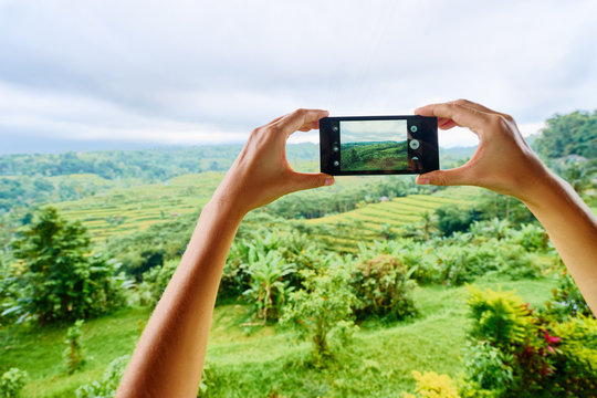 Tourism concept. Woman taking photo of green rice terrace on Bali. Hands holding smartphone.