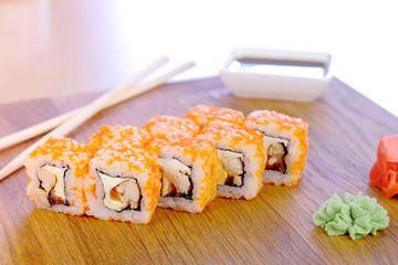 Rolls with fish, shrimps and orange caviar on top served on wooden board with wasabi and soy sauce