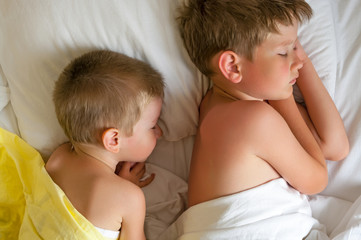 Two sleeping brothers on a bed with white bedclothes.