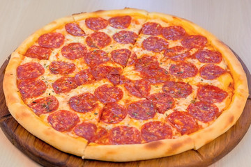 Slicing salami pizza on wooden board on the table. Close-up side view