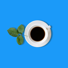 Top view of hot cup coffee on blue background with green leaf