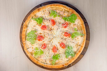 Pizza with chicken and cheese, tomatoes and lettuce on top on wooden board