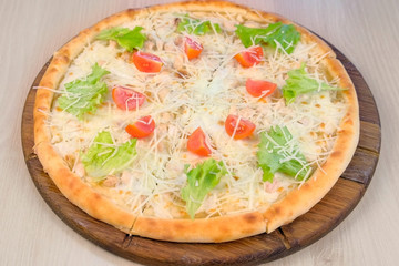 Pizza with chicken and cheese, tomatoes and lettuce on top on wooden board. Side view