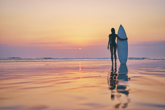 Hobby and vacation. Holiday on the beach. Young woman holding surf board enjoying beautiful sunset.