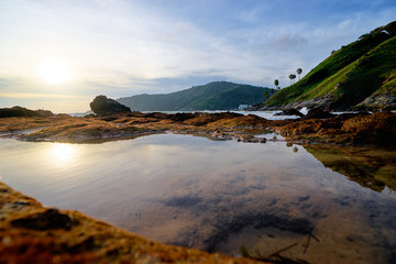 Beautiful sunset landscape with tropical rock seashore and water reflection.