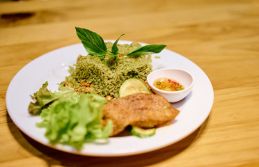 Green rice with fried fish, vegetables and sauce on wooden table.