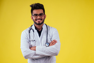 indian male doctor wearing glasses and white cloak in yellow background studio