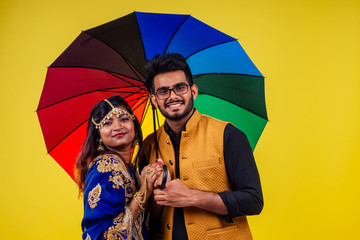 beautiful indian woman in traditional blue india sari and romantic man in kurta together standing under multicolor rainbow umbrella in yellow studio background