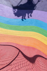 Colourful rainbow rubber floor on an outdoor amusement park with a strong shadow of a playing seat casted. Abstract meaning of fun, enjoy, colourful life and pride.