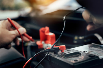 Naklejka premium Car mechanic is using the car battery meter to measure various values and analyze it.