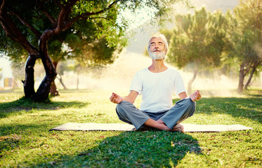 Yoga at park. Senior bearded man in lotus pose sitting on green grass. Concept of calm and meditation.