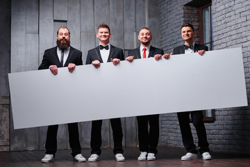 Your advertisement in good hands. Group of handsome young men in tuxedo holding big blank with copy space.