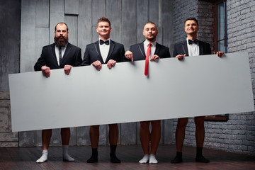 Your advertisement here. Group of handsome fun young men in pants and socks holding big blank with...