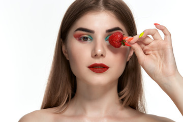 Closeup portrait of a beautiful young woman with bright color make-up holding strawberry close to face.