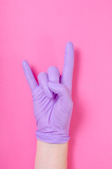 Human hand wearing purple, medical glove makes sign of metal hand