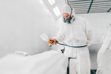 Man painting car body parts in paint booth.