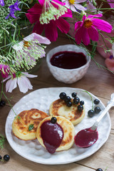 Breakfast of quark pancakes, black currant custard, currants and a bouquet of wild flowers on a wooden background.