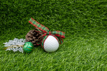 Golf ball with Christmas ribbon and Christmas ornament on green grass