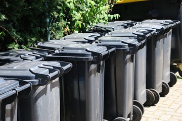 many black garbage cans are standing in a row