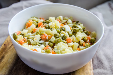 Russian salad Olivier with potato carrot green peas on the board and gray background