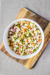Russian salad Olivier with potato carrot green peas ham on the board and gray background