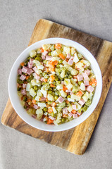 Russian salad Olivier with potato carrot green peas ham on the board and gray background