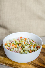 Russian salad Olivier with potato carrot green peas ham on the board and gray background