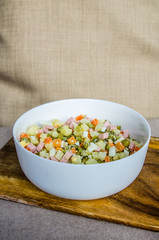 Russian salad Olivier with potato carrot green peas ham on the board and gray background