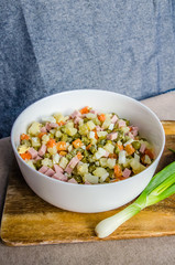 Russian salad Olivier with potato carrot green peas ham on the board and gray background