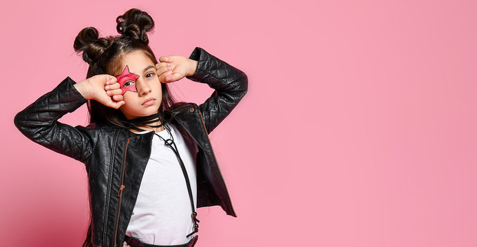 Portrait of a hipster punk girl - dressed in a leather jacket and skirt, black knee-highs and a white T-shirt, with a funny hairstyle and a makeup painted star on the face, points to the head.