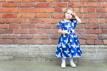 Girl in a blue dress against a brick wall